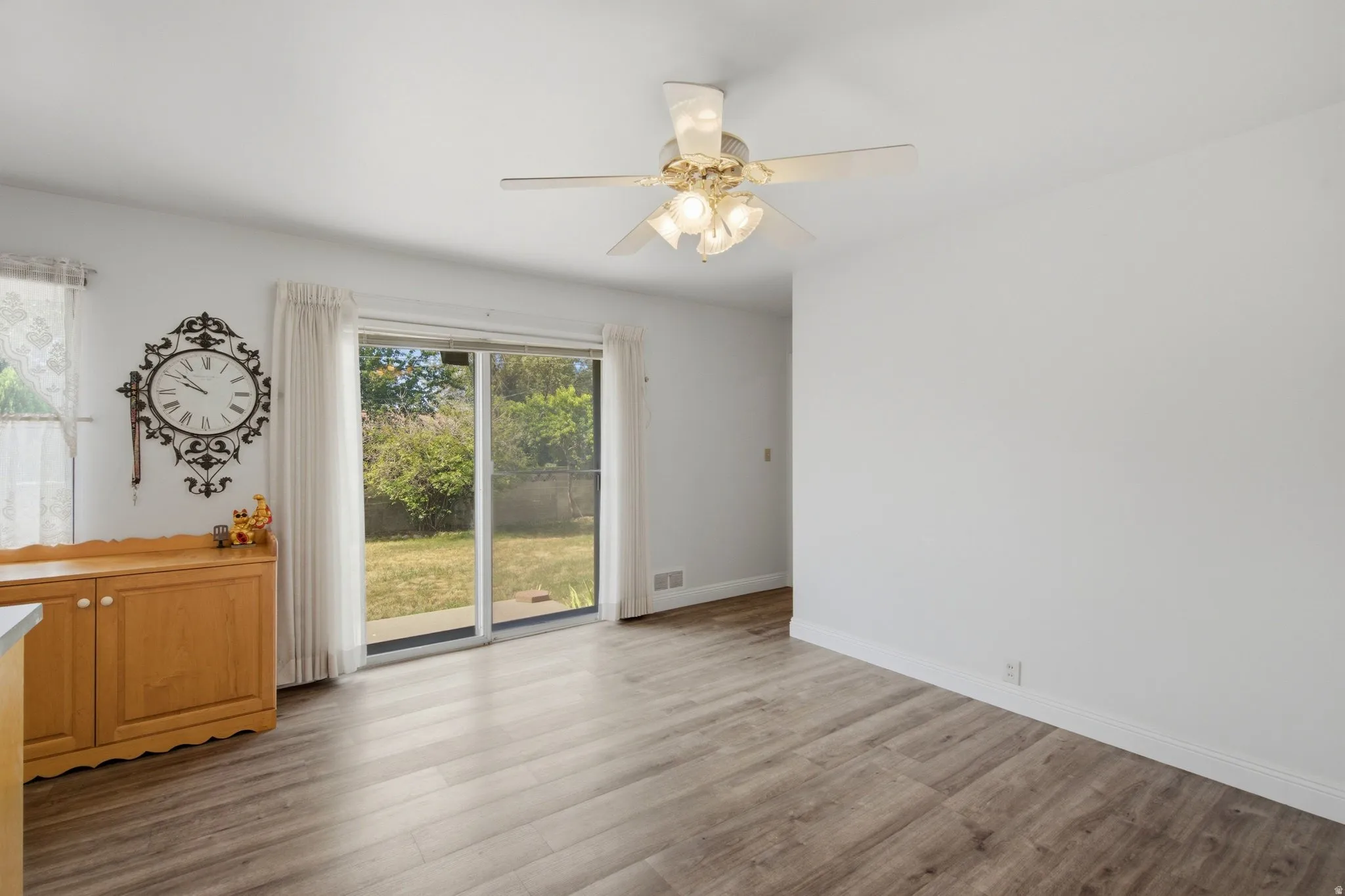 Sliding glass door leading to a private outdoor area, wood-finish flooring, ceiling fan with integrated lighting, white baseboards, and neutral wall tones