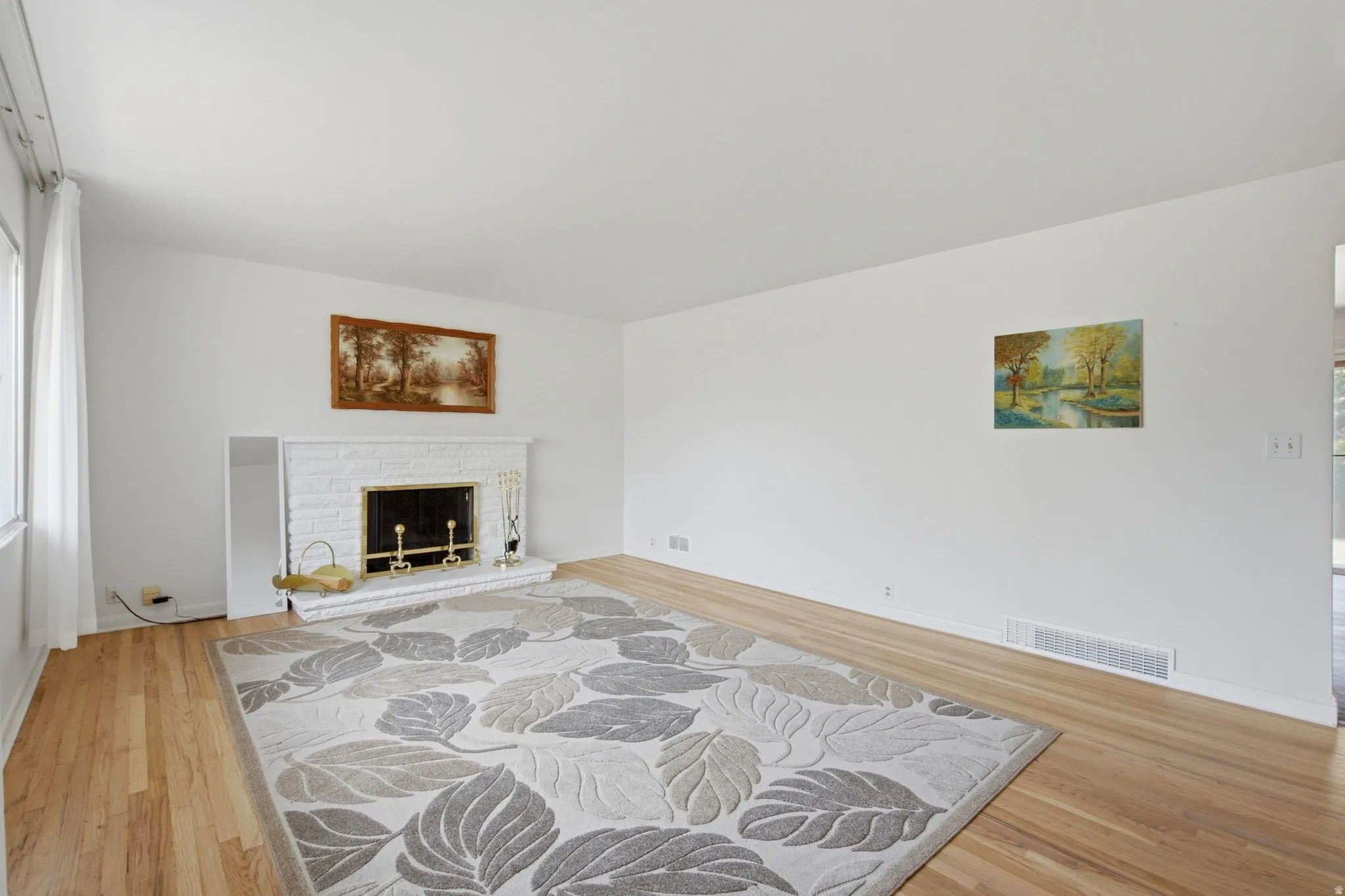 Living area featuring light wood-finish flooring, white painted walls, and a white brick fireplace with a brass firebox