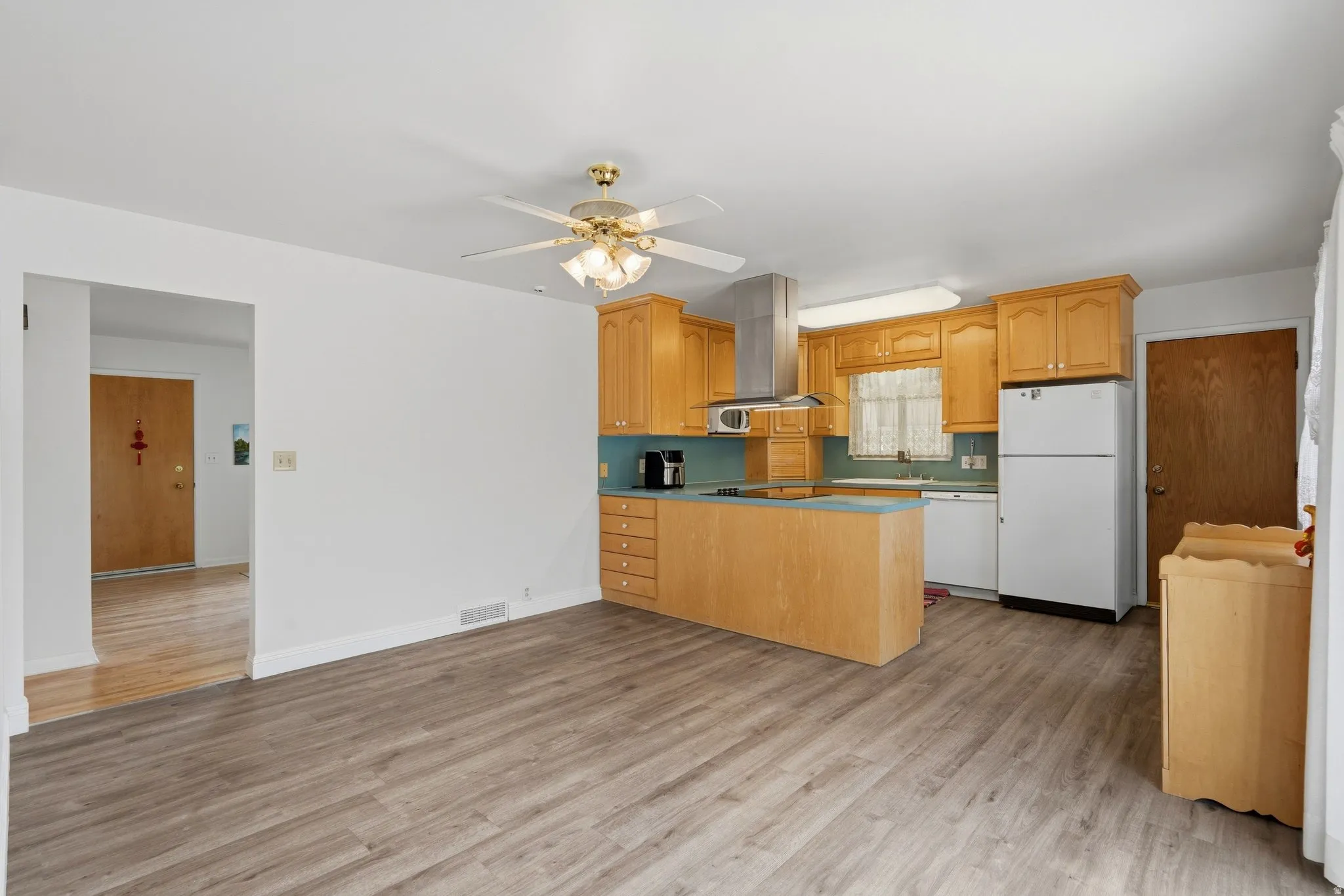 Kitchen featuring wood-finish cabinetry, stainless steel range hood, built-in microwave, and a ceiling fan