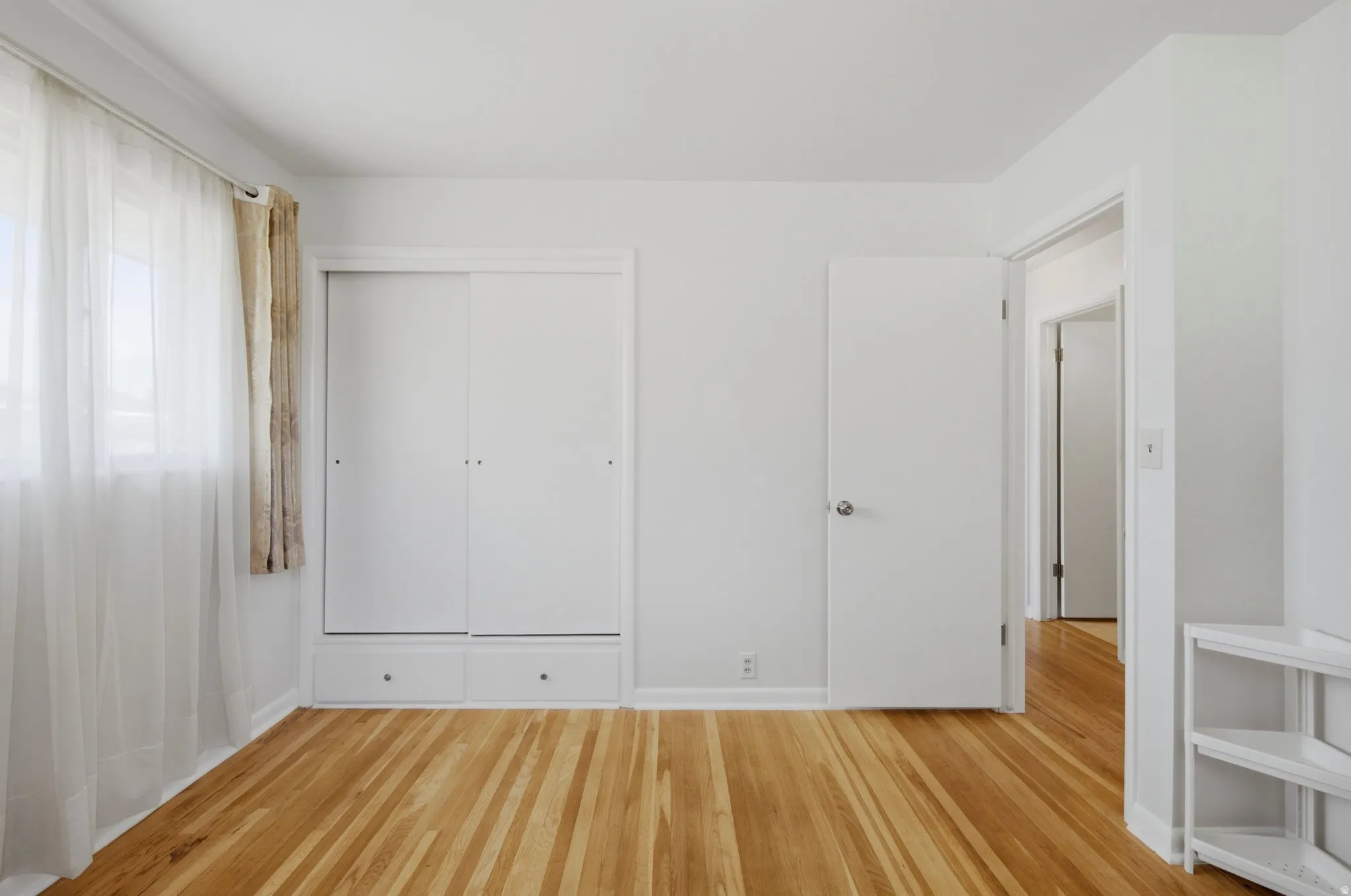Light-filled interior featuring hardwood flooring, white walls, and a built-in closet with sliding doors and integrated drawers