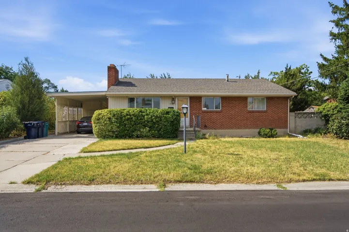 Brick and siding exterior featuring a covered carport, mature front yard landscaping, and a concrete driveway