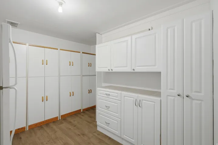 White cabinetry with varied storage options, wood-finish flooring, and a neutral countertop