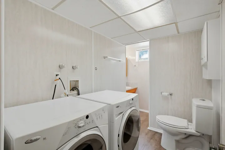 Dedicated laundry area featuring a white front-load washer and dryer, adjacent to a full bathroom with wood-finish flooring