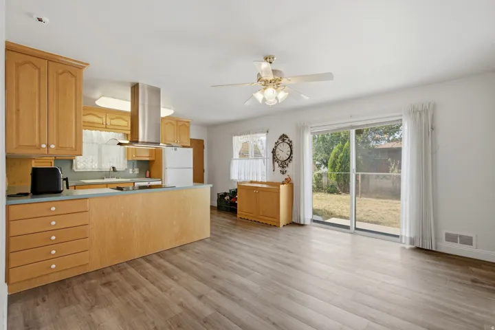 Kitchen and living area featuring wood-finish flooring, wood cabinetry, a stainless steel range hood, a ceiling fan, and sliding glass doors to the exterior