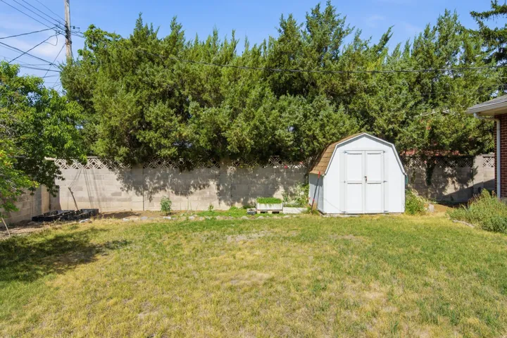 Expansive backyard featuring a storage shed with a gambrel roof, mature trees along the perimeter, and a concrete block fence