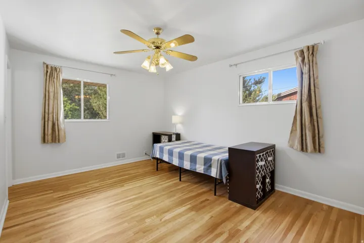 Bedroom featuring wood-finish flooring, two windows, a ceiling fan with integrated lighting, and white walls