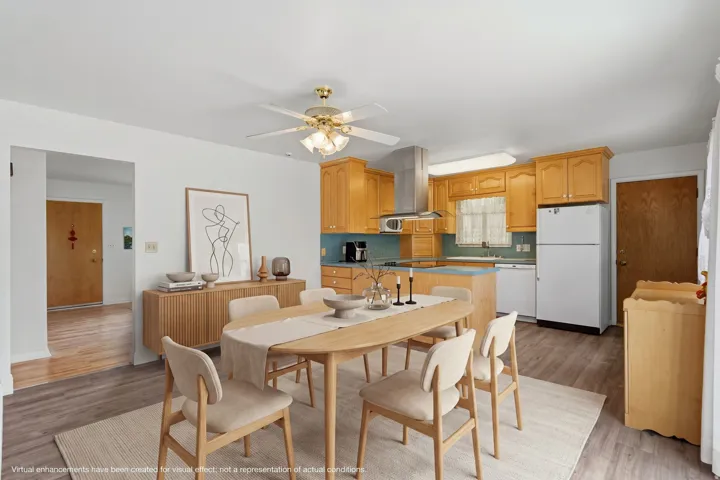Open-concept kitchen and dining area featuring wood-finish flooring, warm-toned cabinetry, light blue backsplash, and a contemporary ceiling fan