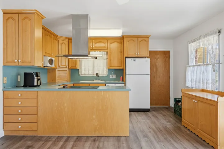 Kitchen featuring wood cabinetry, a stainless steel range hood, built-in cooktop, light blue countertops, and wood-finish flooring