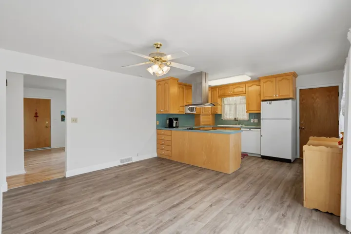 Kitchen featuring wood-finish cabinetry, stainless steel range hood, built-in microwave, and a ceiling fan
