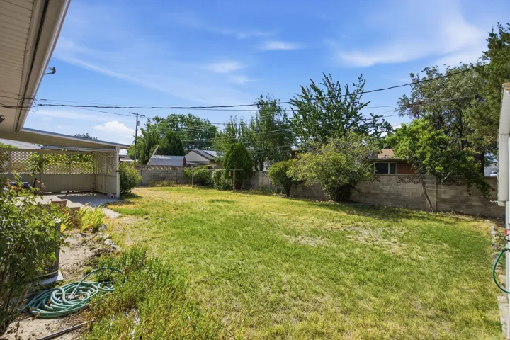 Expansive backyard featuring a concrete patio with a lattice privacy wall, a large grass area, and a concrete block retaining wall