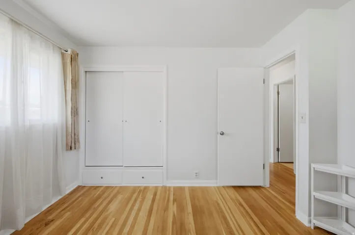 Light-filled interior featuring hardwood flooring, white walls, and a built-in closet with sliding doors and integrated drawers