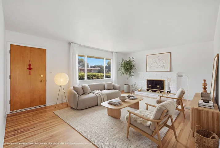 Bright living space featuring natural wood-finish flooring, a white brick fireplace, and ample natural light from a large window