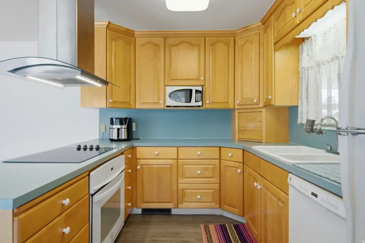 Kitchen with wood cabinetry, light blue countertops, and a full suite of appliances including an integrated cooktop, wall oven, and microwave