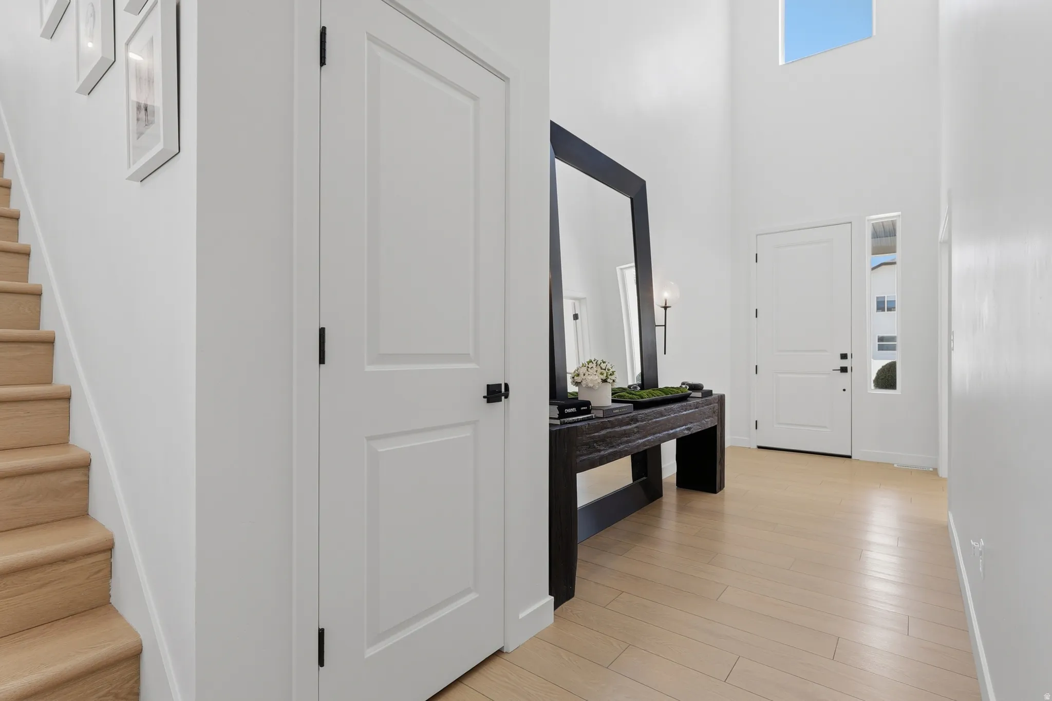 Bright foyer featuring a double-height ceiling, light wood-finish flooring, a contemporary front door with sidelight, and a light wood staircase
