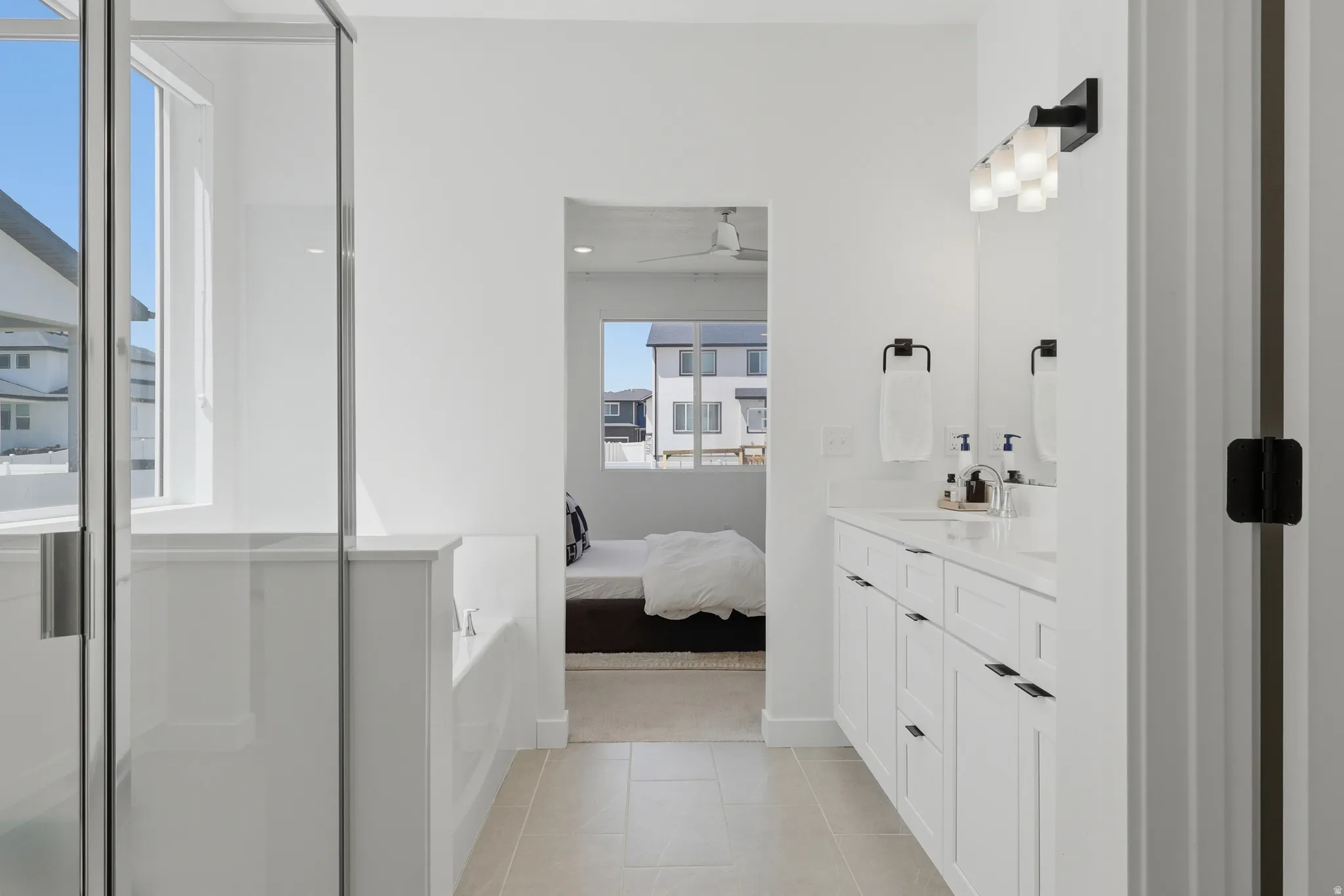 Bathroom featuring a double vanity with white cabinetry and a light-toned countertop, a frameless glass shower enclosure, and neutral tile flooring