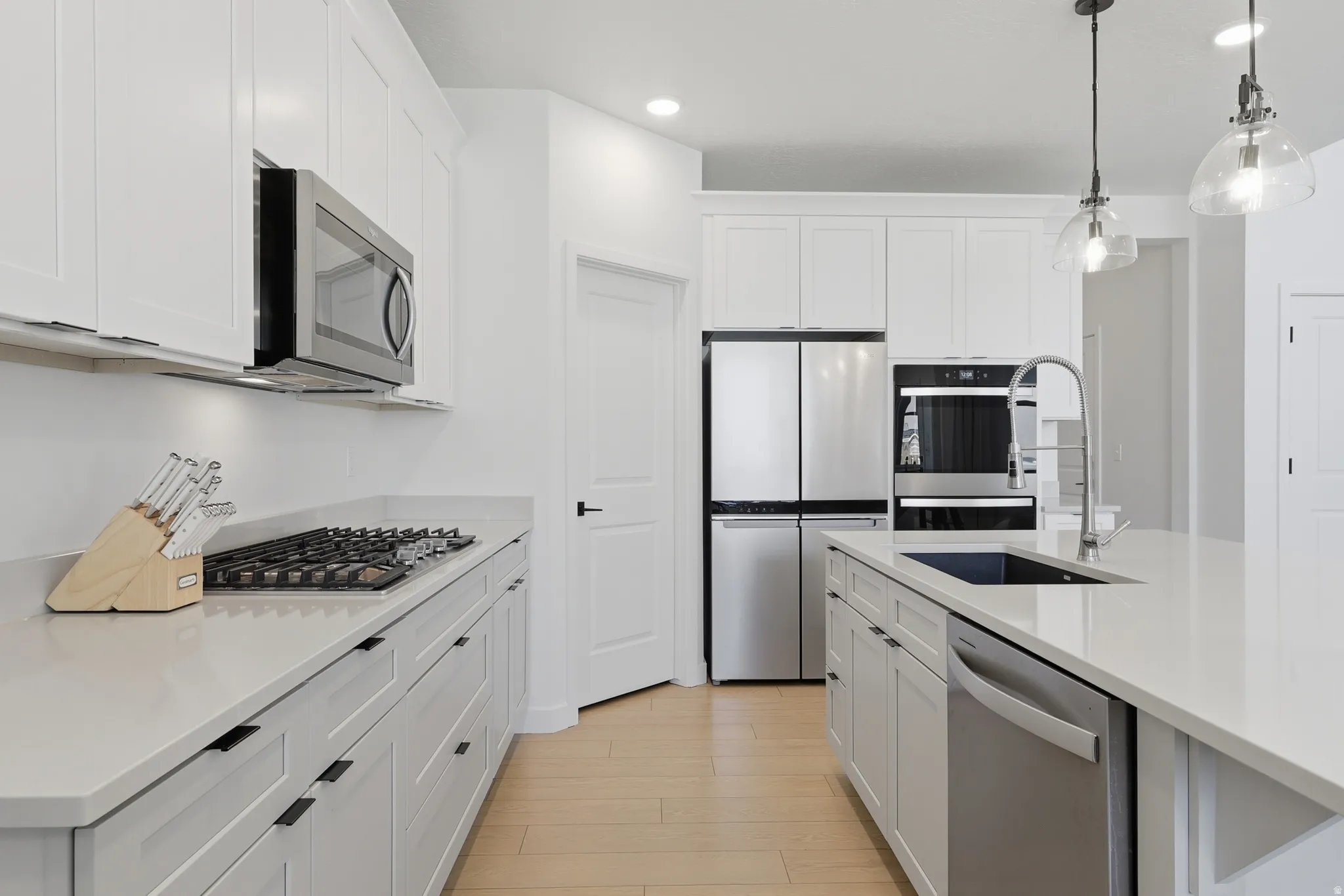 Bright kitchen featuring white shaker cabinetry, stainless steel appliances, a gas cooktop, light-toned countertops, and wood-finish flooring