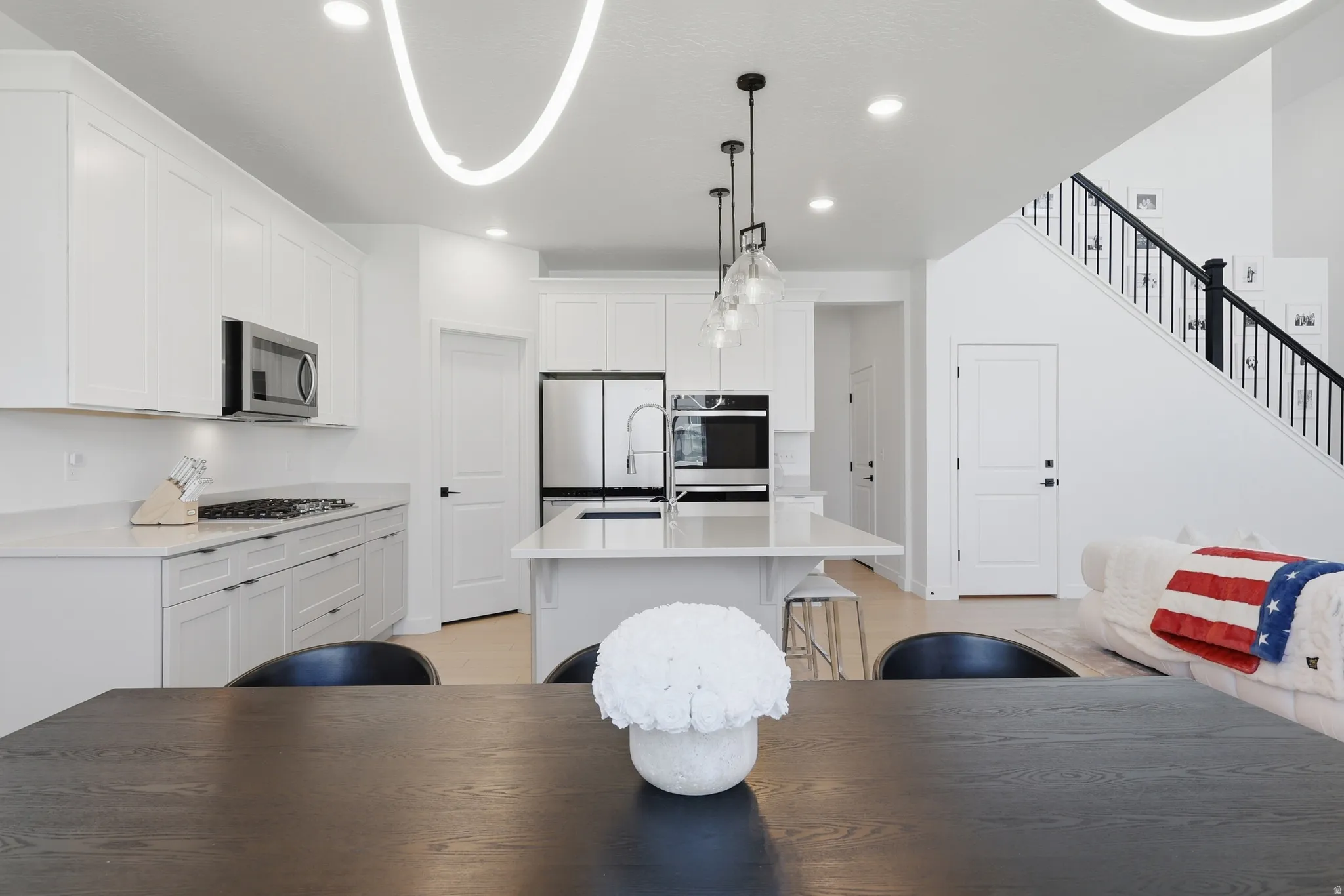 Contemporary open-concept kitchen featuring white shaker cabinetry, stainless steel appliances, a center island with pendant lighting, and light-tone flooring