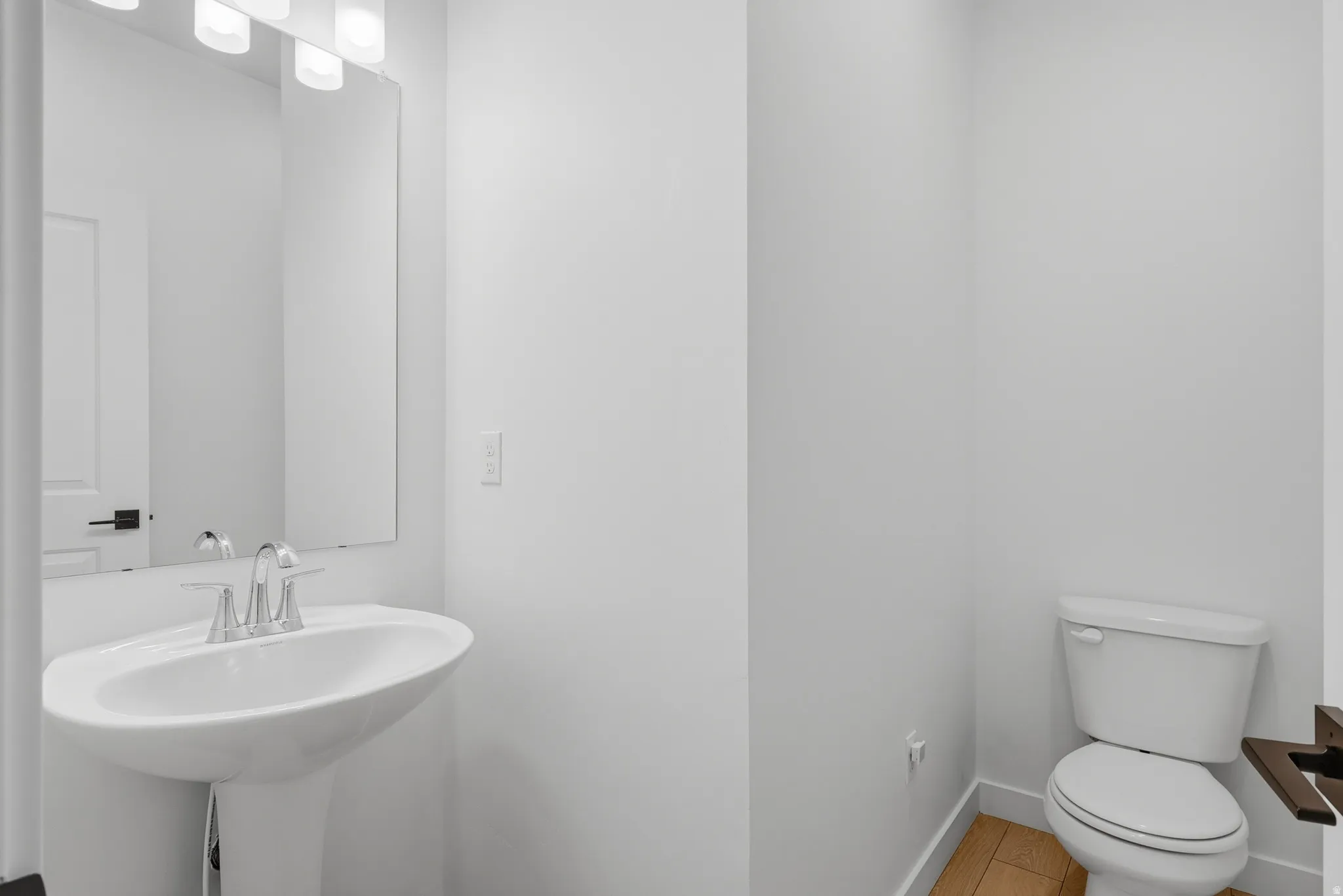 Pedestal sink with chrome faucet, large vanity mirror, and three-light fixture