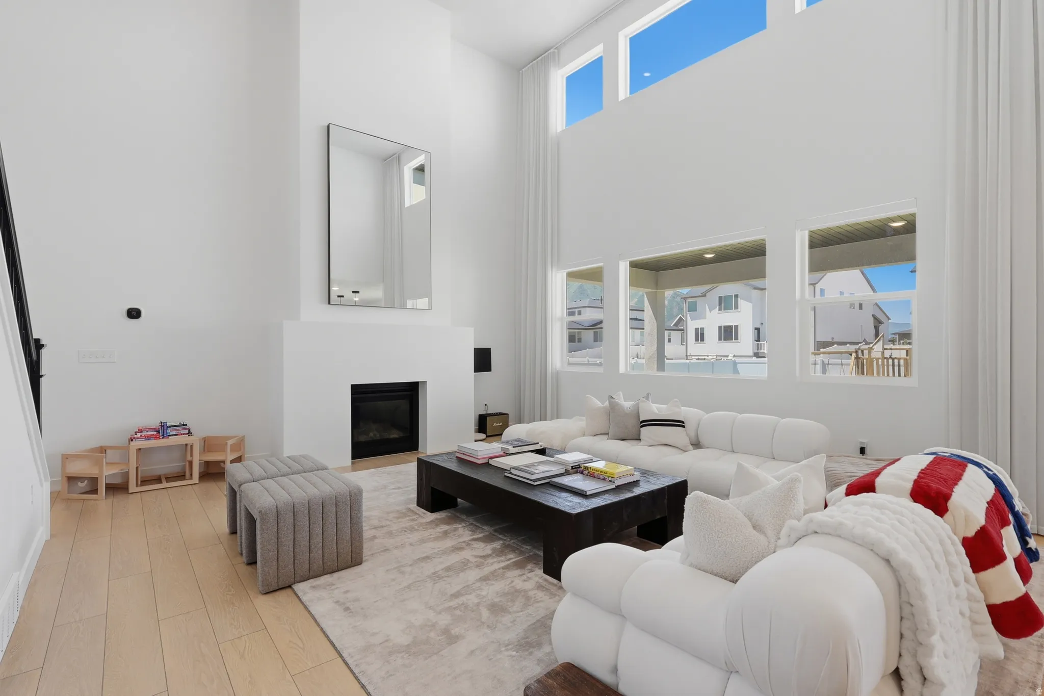 Two-story living area featuring a prominent fireplace with a sleek black insert, light wood-finish flooring, and multiple high windows