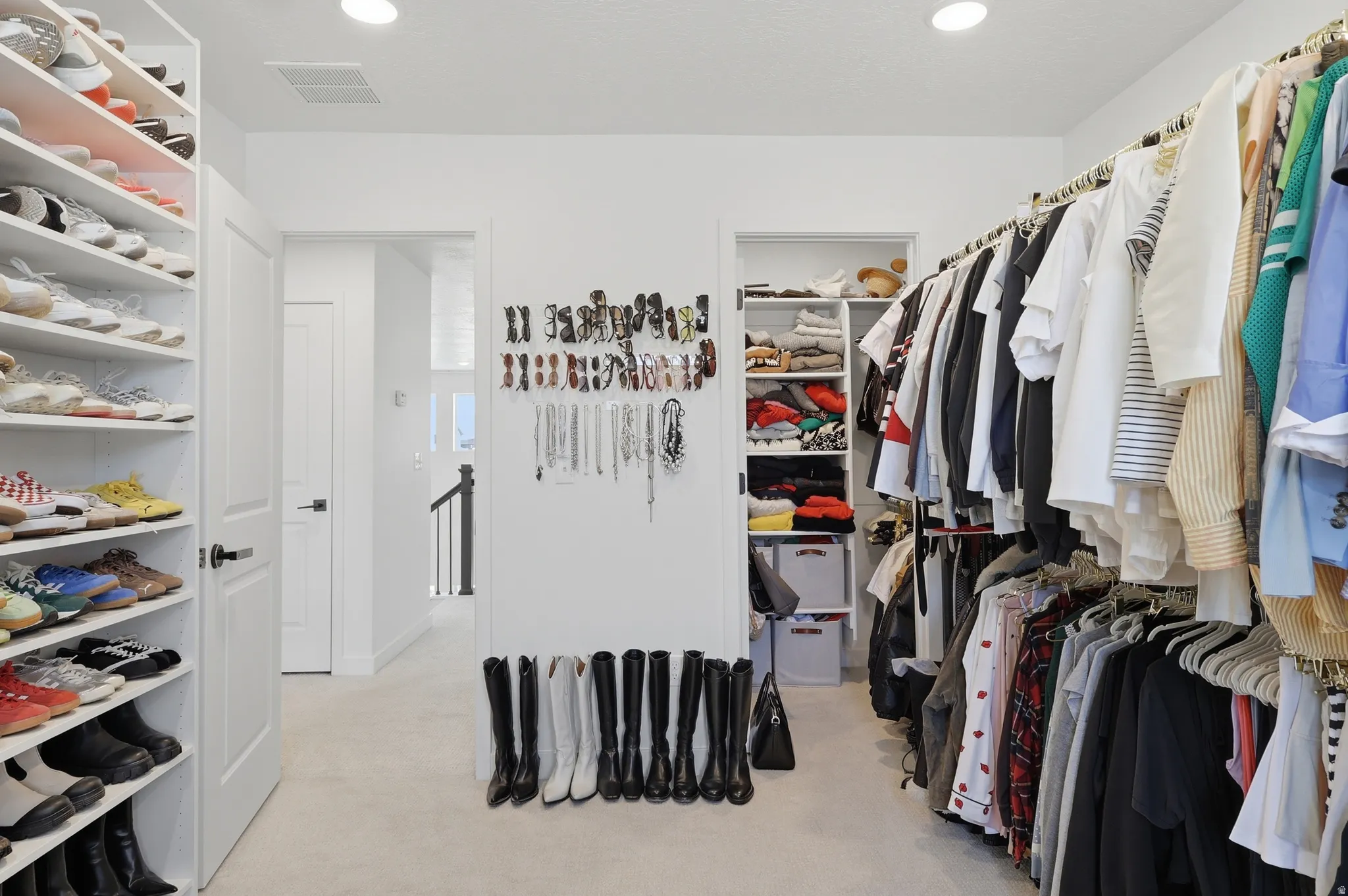 Spacious walk-in closet featuring extensive built-in shelving, multiple hanging rods, recessed lighting, and light-toned carpeting