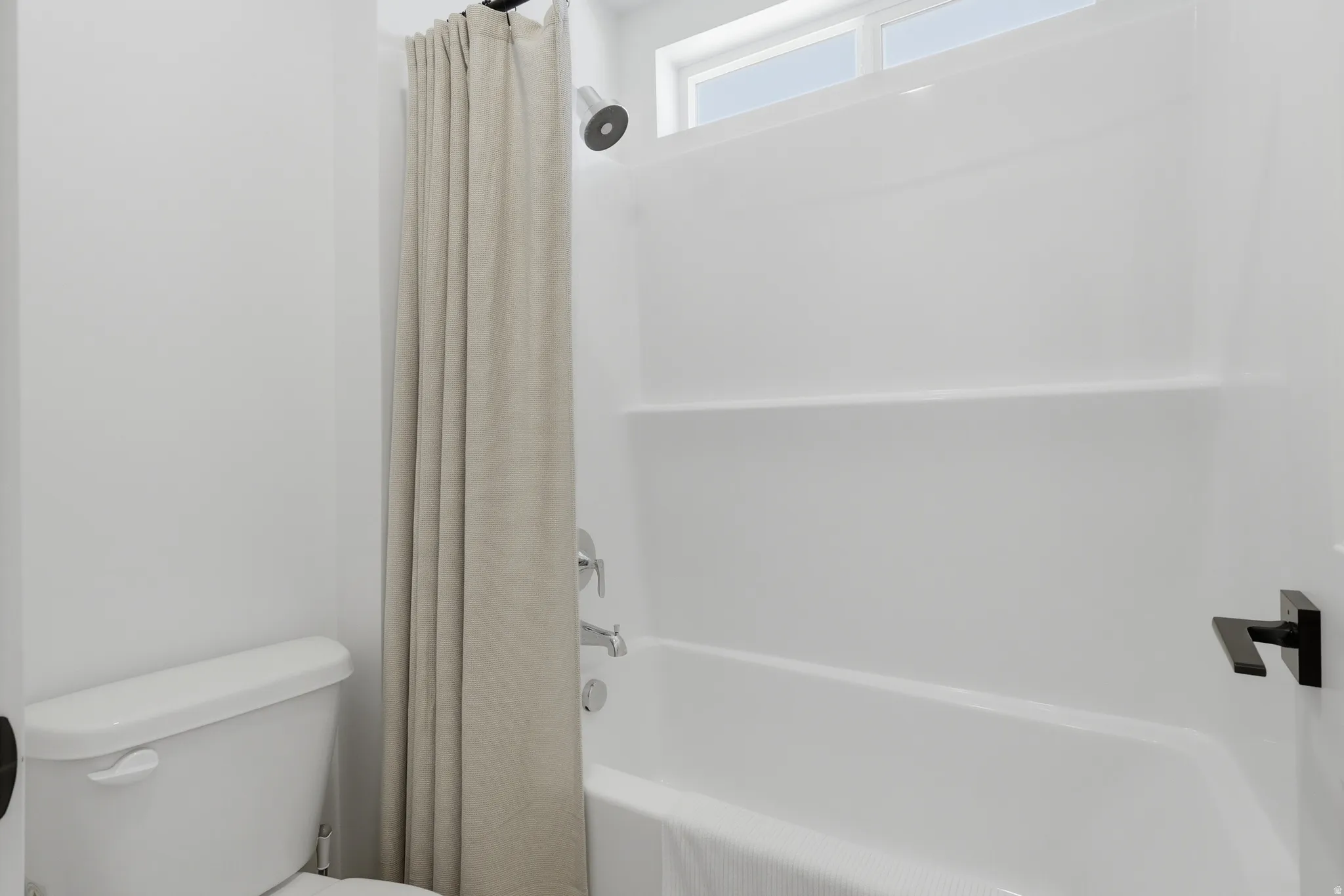 White tub and shower combination featuring a matte black shower head and faucet hardware