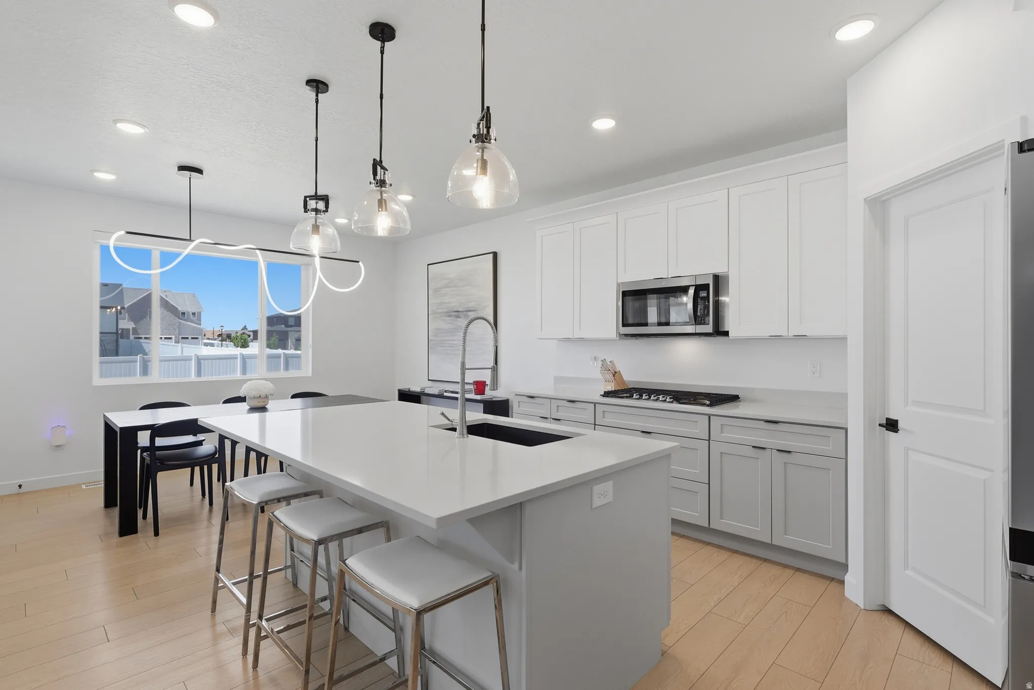 Contemporary kitchen featuring a large central island with seating, light wood-finish flooring, white upper cabinetry, and stainless steel appliances including a built-in microwave and gas range