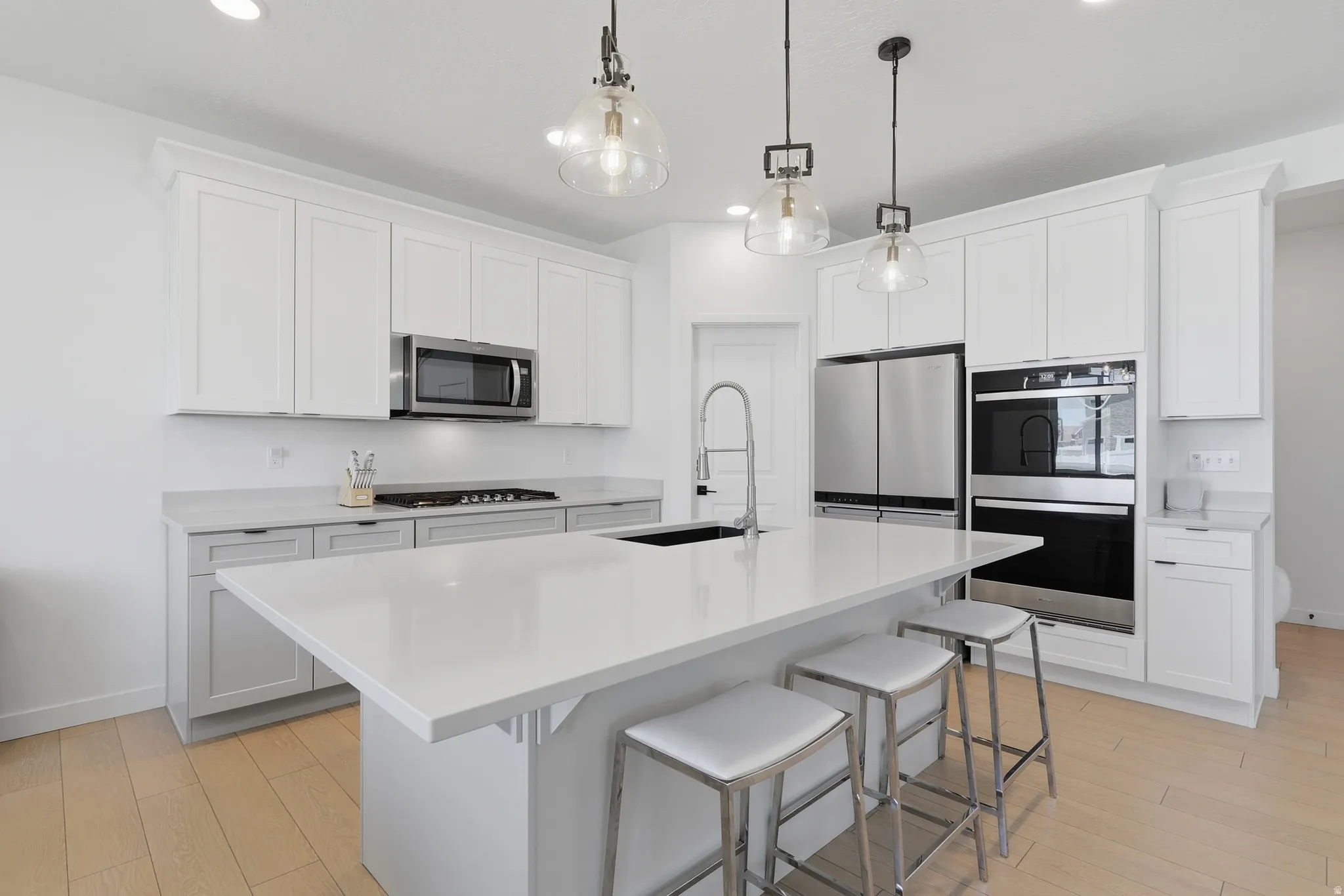 Kitchen featuring a large central island with seating, white shaker-style cabinetry, stainless steel appliances, and wood-finish flooring