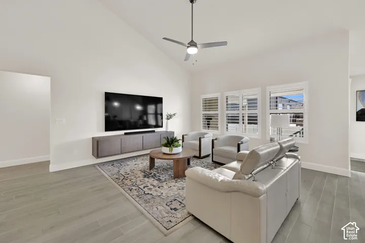 Living area featuring vaulted ceilings, wood-finish flooring, a contemporary ceiling fan, and multiple windows with plantation shutters