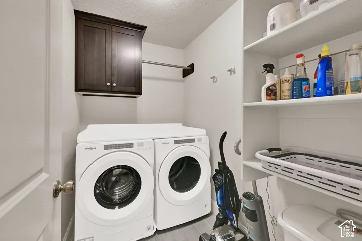 Dedicated laundry space featuring a dark wood finish upper cabinet, a chrome hanging rod, and light-colored flooring