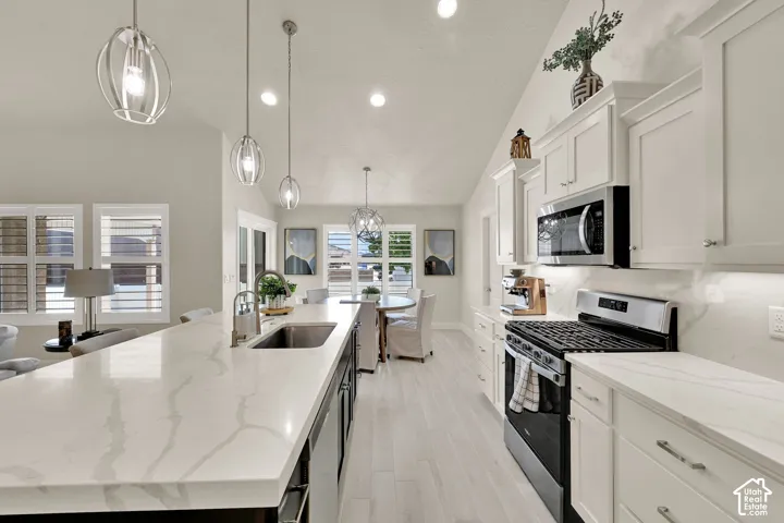 Spacious kitchen featuring a large island with an undermount sink, pendant lighting, white shaker cabinetry, stainless steel appliances, and light wood-finish flooring