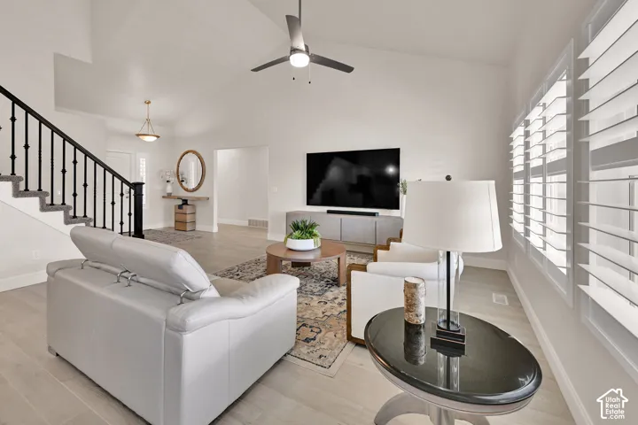 Vaulted ceiling living area featuring light wood-finish flooring and multiple windows with plantation shutters