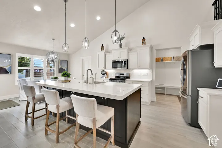 Modern kitchen featuring a large island with a light-toned countertop, white cabinetry, integrated stainless steel appliances, and wood-finish flooring