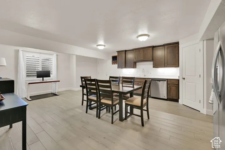 Open-concept room featuring wood-finish flooring, a kitchen area with dark wood cabinetry and stainless steel appliances, recessed ceiling lighting, and a window with white blinds