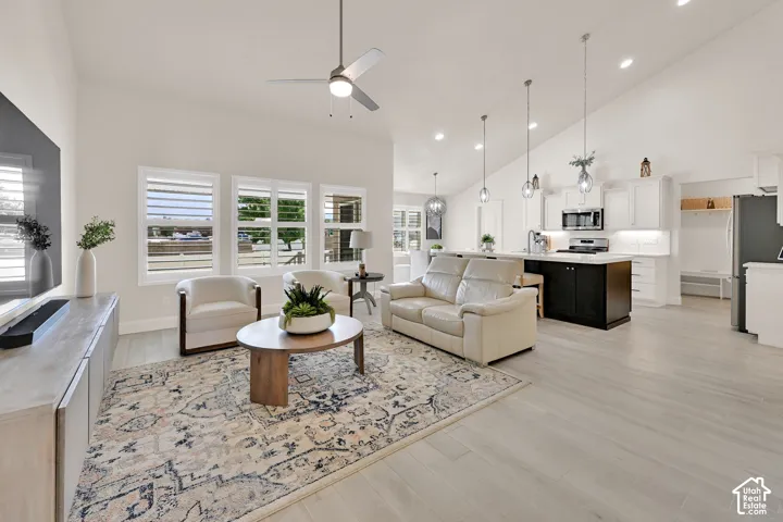 Bright interior featuring vaulted ceilings, light wood-finish flooring, white plantation shutters, and a kitchen island with pendant lighting