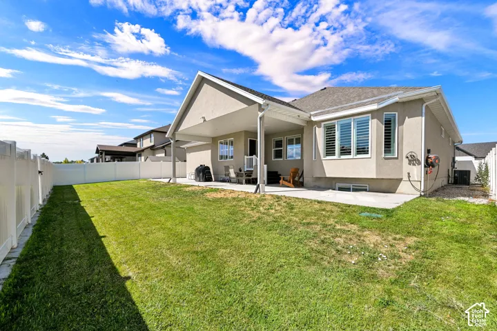 Spacious backyard featuring a manicured lawn, full vinyl privacy fencing, and a covered patio area with an additional concrete pad