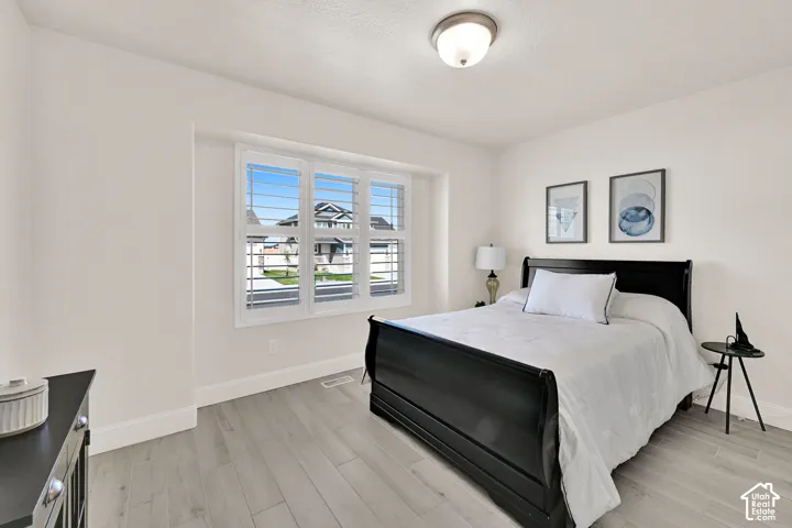 Bright room featuring a large window with white plantation shutters, light gray wood-finish flooring, a neutral wall color, and a flush mount ceiling light fixture