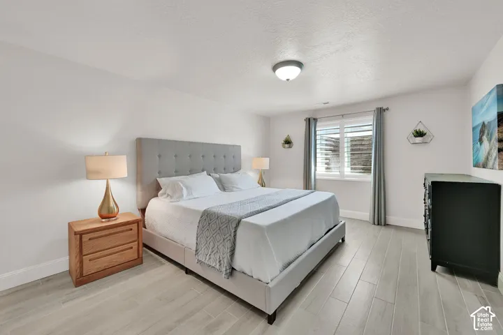 Bedroom featuring light wood-finish flooring, a window with horizontal blinds, and a built-in flush-mount ceiling light