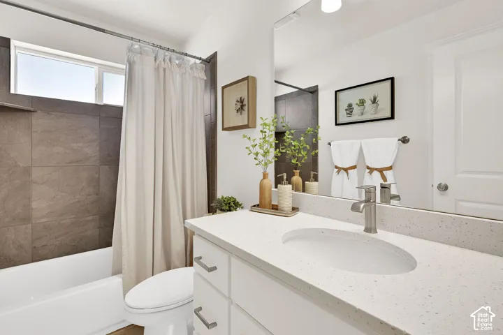 Bathroom featuring a white vanity with integrated sink, a large wall-mounted mirror, and a shower/tub combination with dark tile surround and an upper window