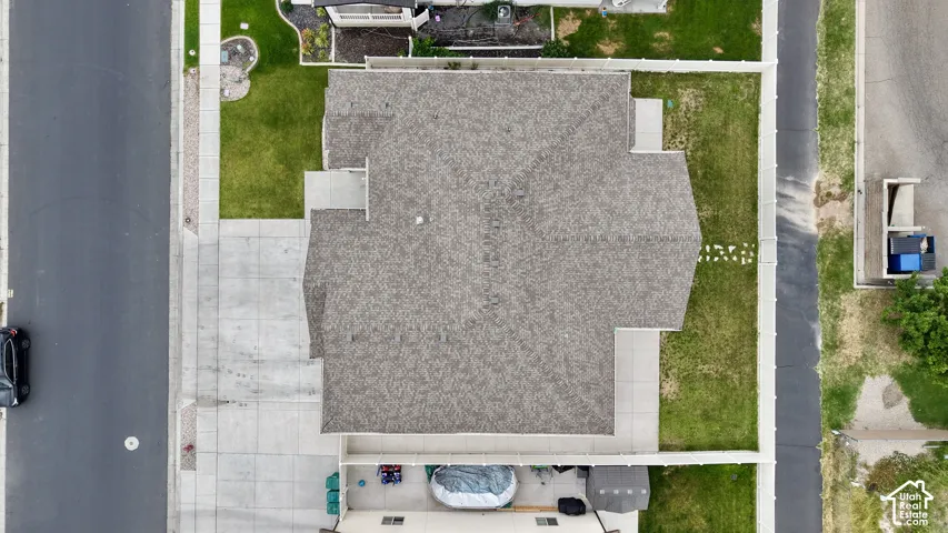 Property featuring a shingled roof, surrounding green lawns, and concrete driveways with sidewalk access