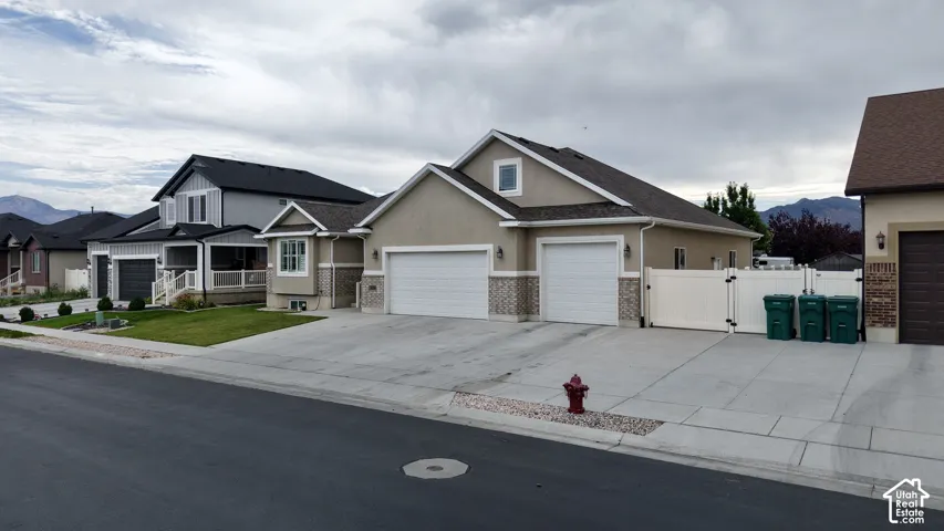 Contemporary stucco and stone exterior featuring a two-car garage, a well-maintained lawn, and a light-colored privacy fence