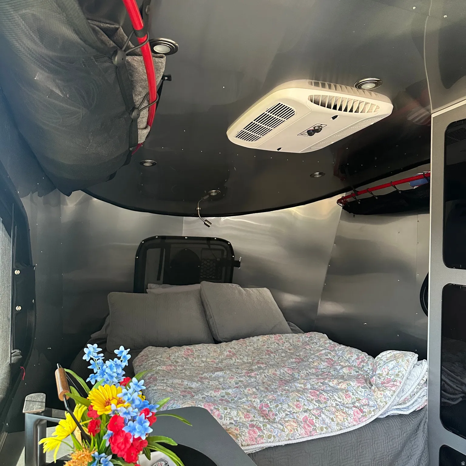 Sleeping area featuring polished metal walls, overhead climate control unit, integrated ceiling lighting, and a built-in window with mesh screen