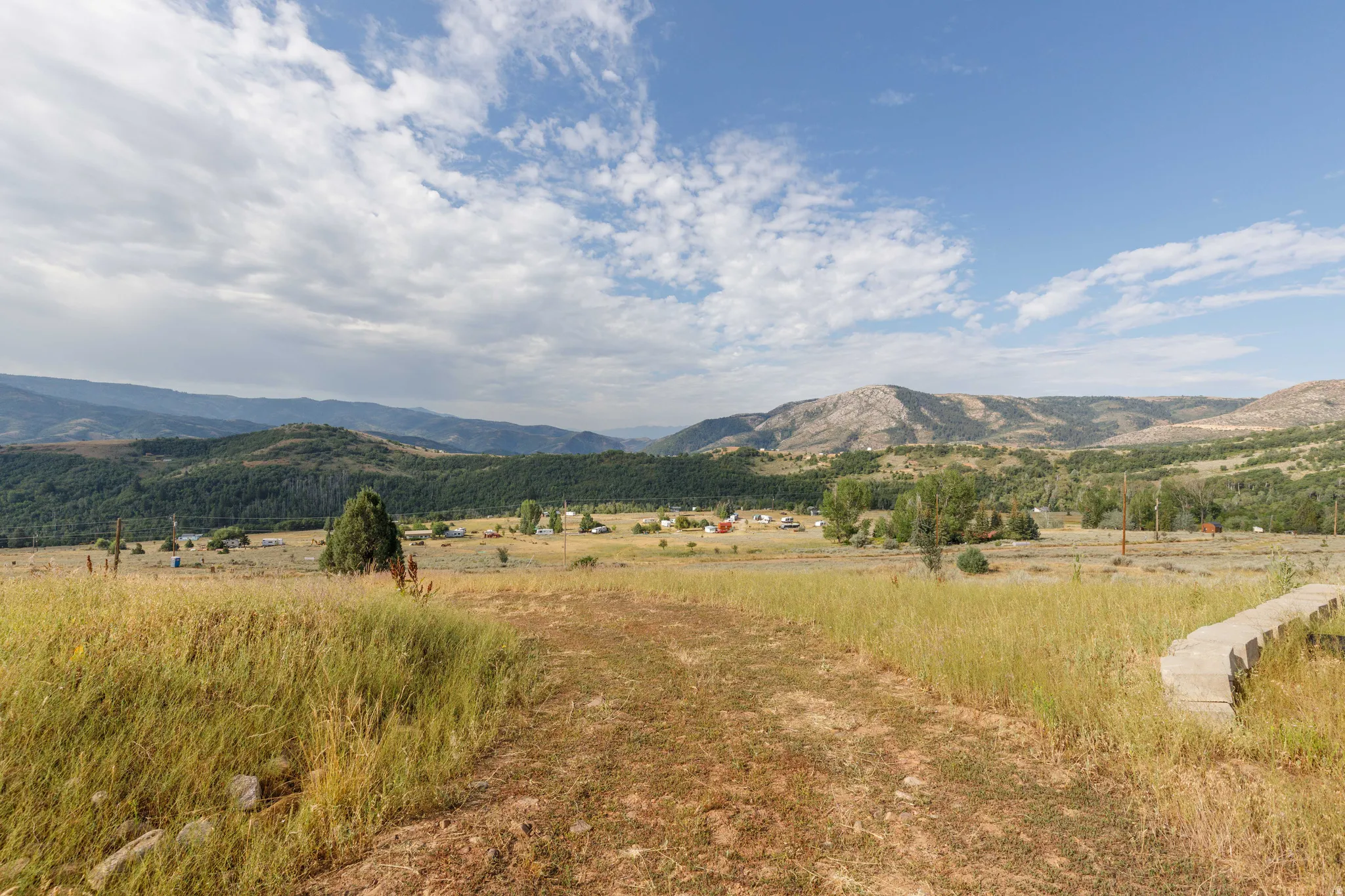 Expansive natural landscape featuring rolling hills, mature trees, and mountainous terrain under a clear sky