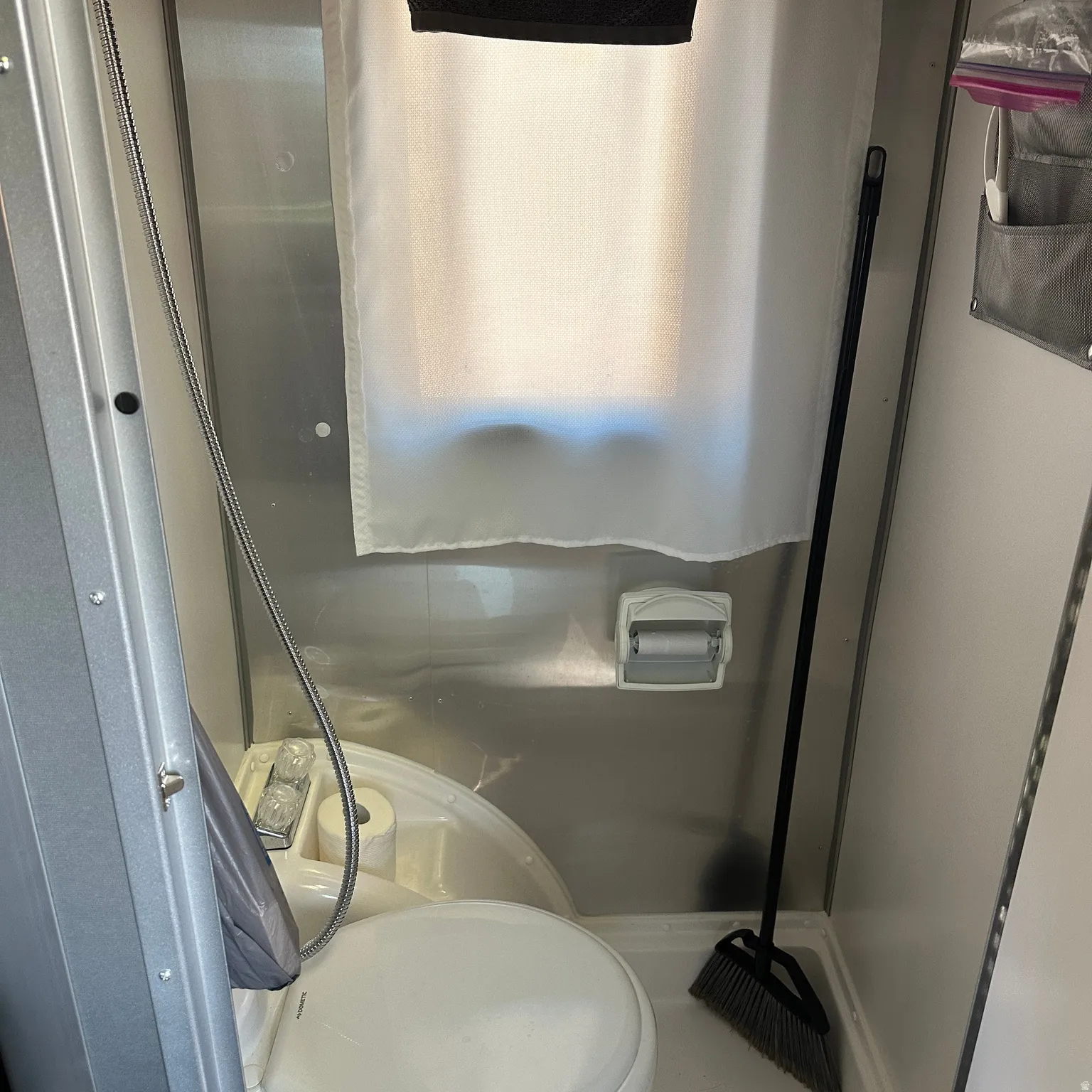 Compact bathroom featuring a white toilet, integrated sink basin, chrome shower hose, and a wall-mounted toilet paper holder