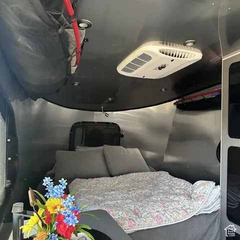 Sleeping area featuring polished metal walls, overhead climate control unit, integrated ceiling lighting, and a built-in window with mesh screen