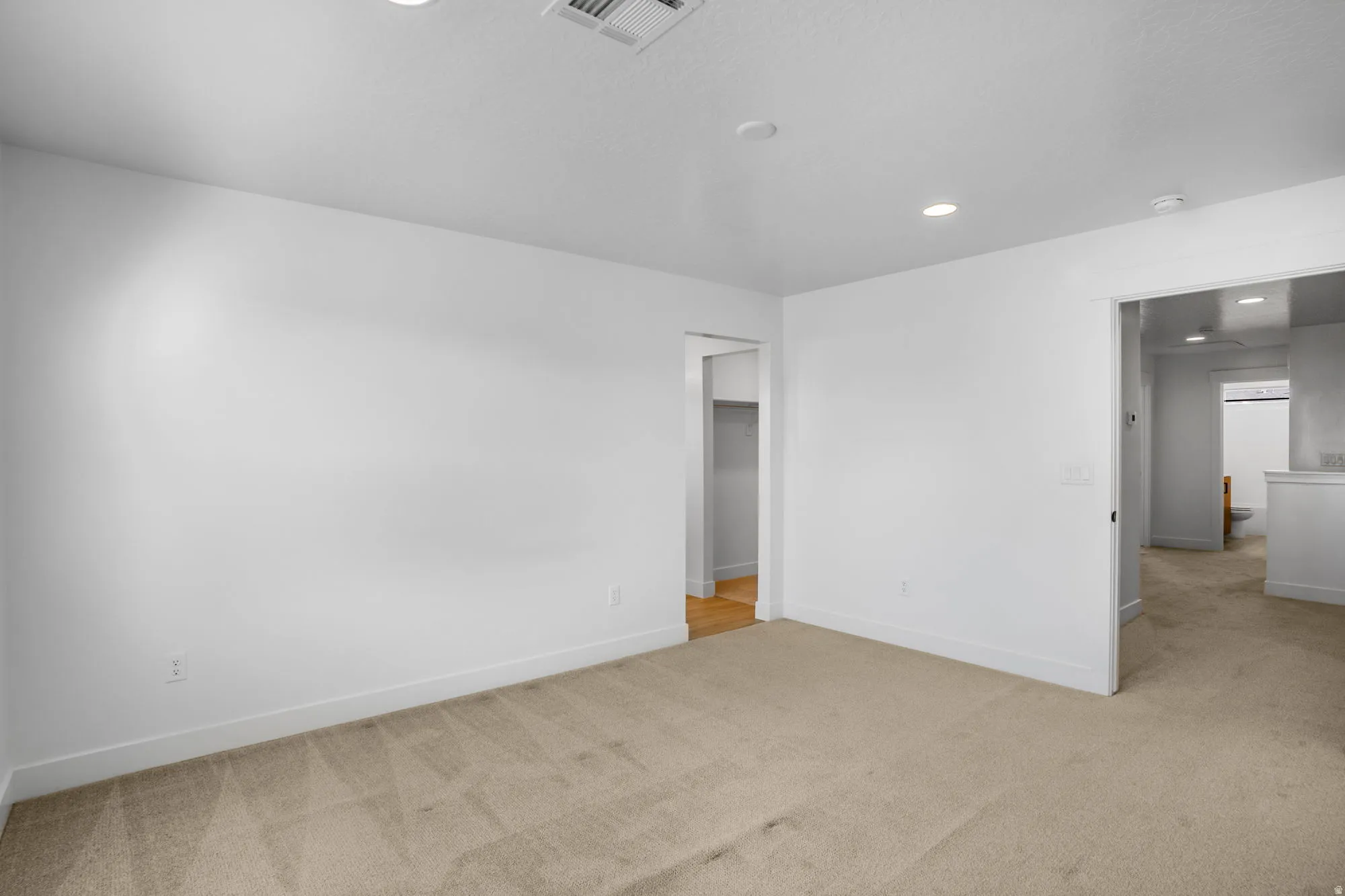 Spacious interior room featuring clean white walls, recessed ceiling lighting, and neutral wood-finish flooring