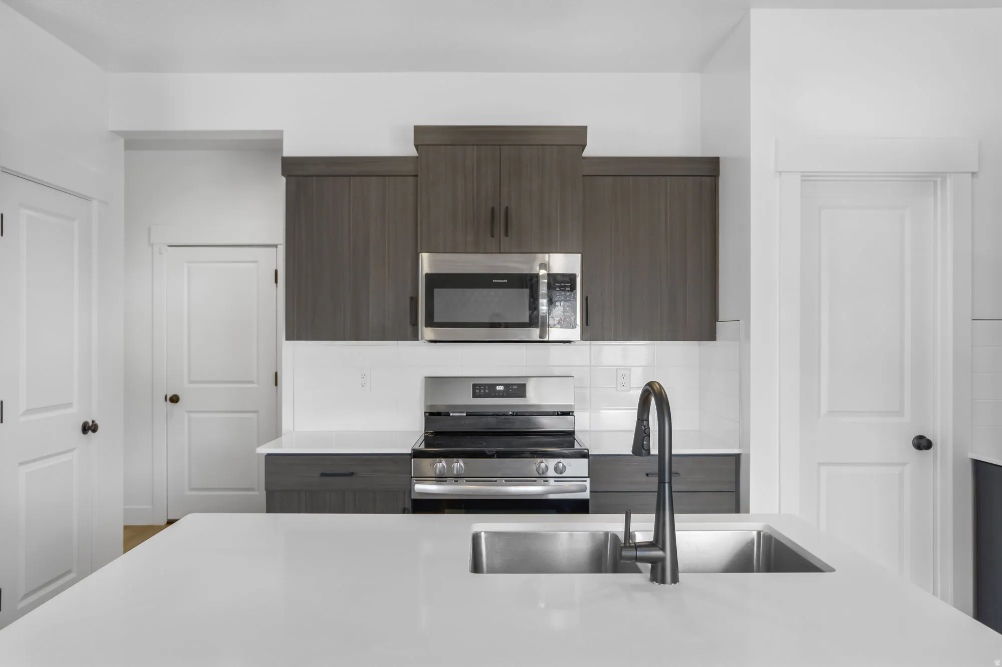 Modern kitchen featuring a white quartz countertop with waterfall edge, stainless steel undermount sink with contemporary matte black faucet, and integrated appliances including a microwave, cooktop, and wall-mounted range hood