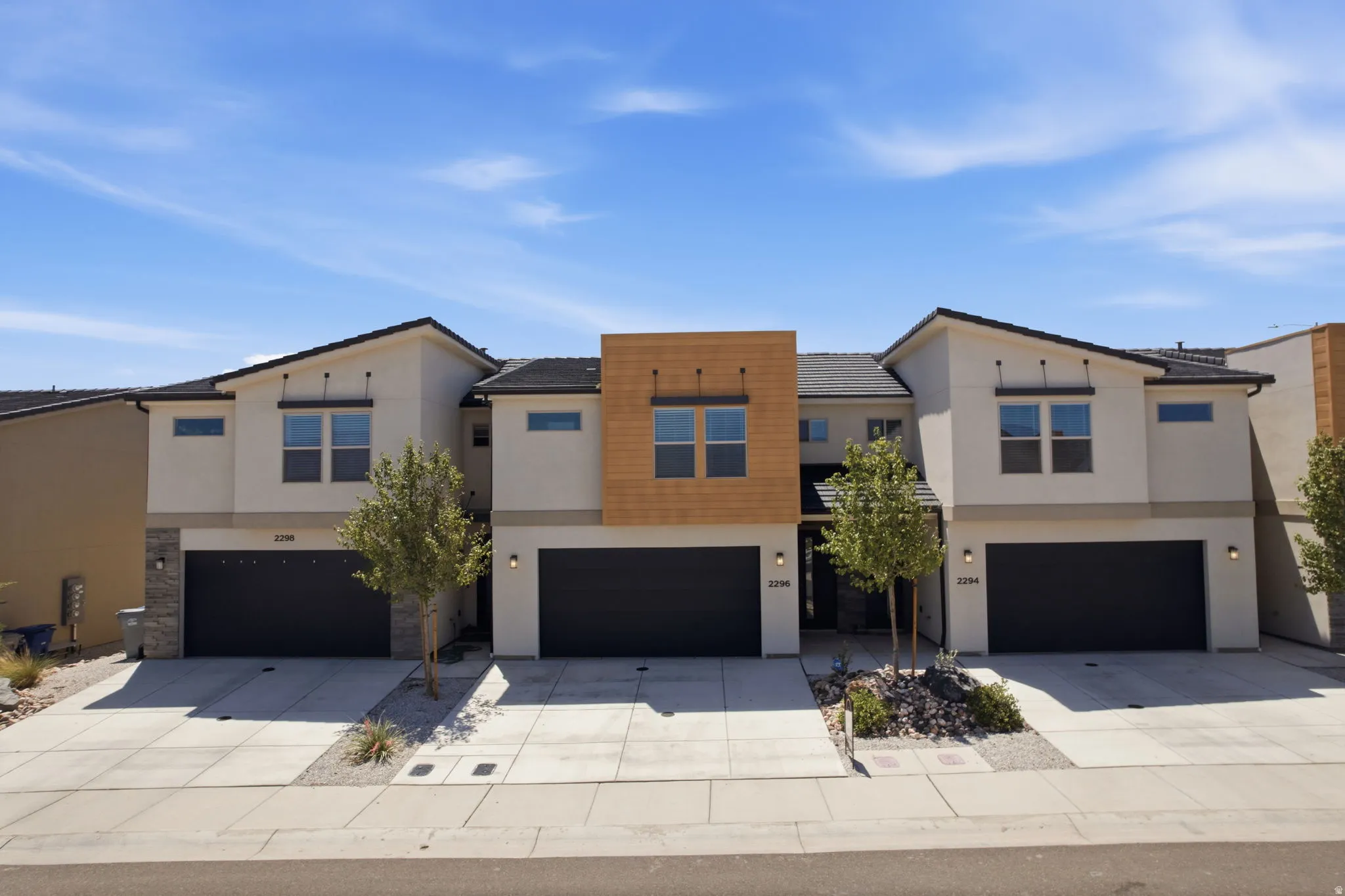 Contemporary multi-unit residence featuring stucco and wood-finish siding, black garage doors, and a tiled roof
