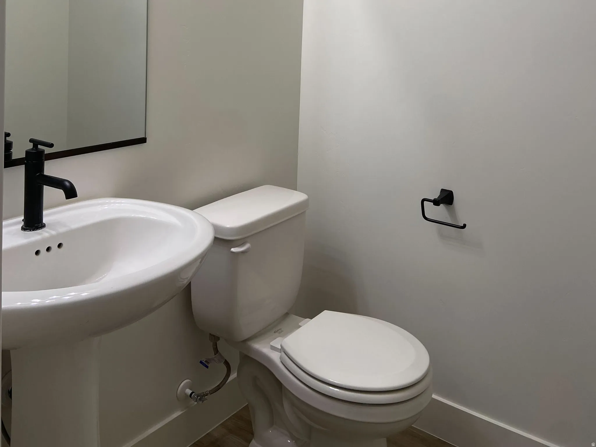 Powder room featuring a pedestal sink with a matte black faucet, a rectangular mirror, and a three-bulb vanity light fixture