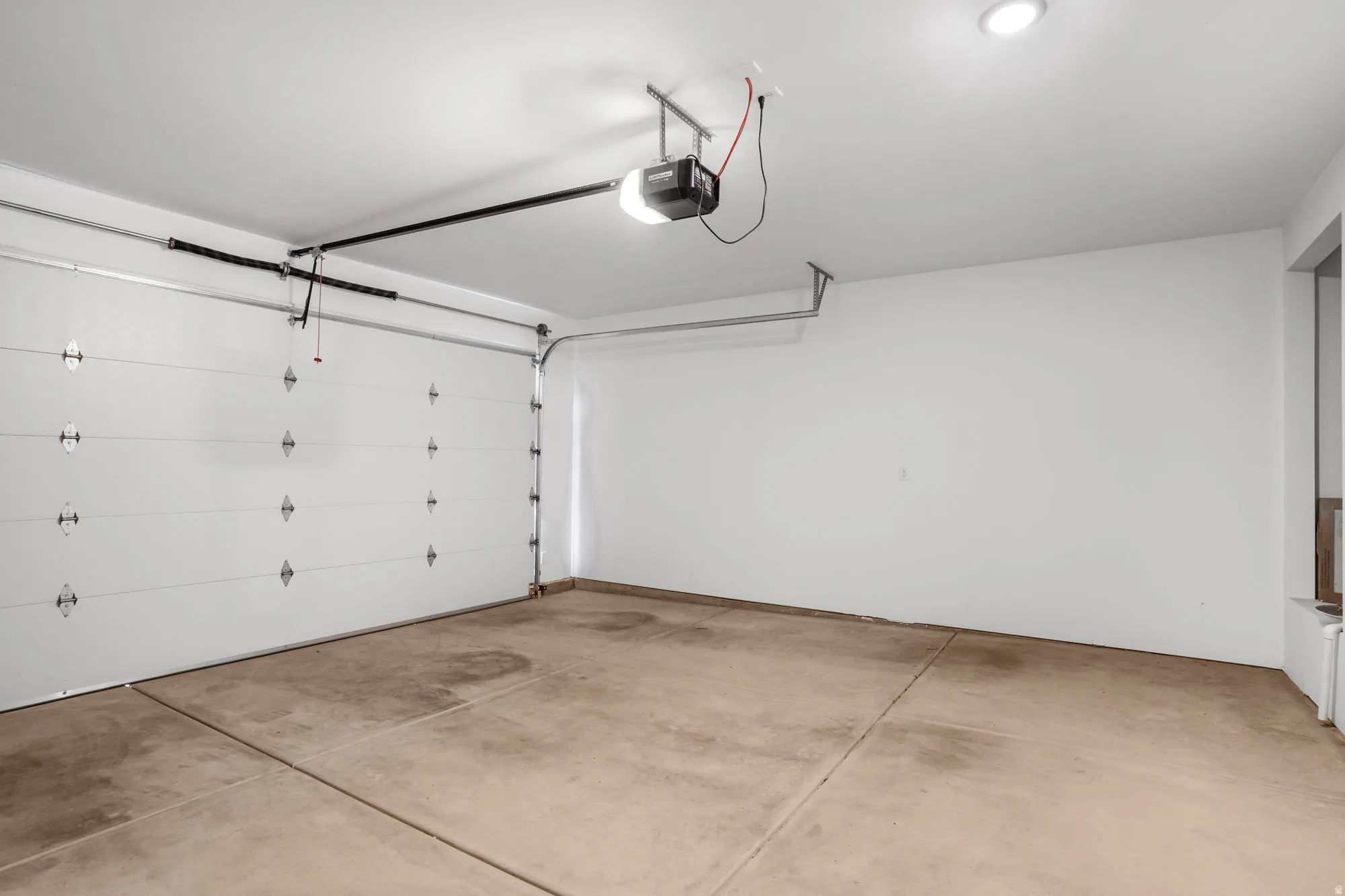 Spacious garage featuring a concrete floor, white painted walls, and a white paneled garage door with an automatic opener