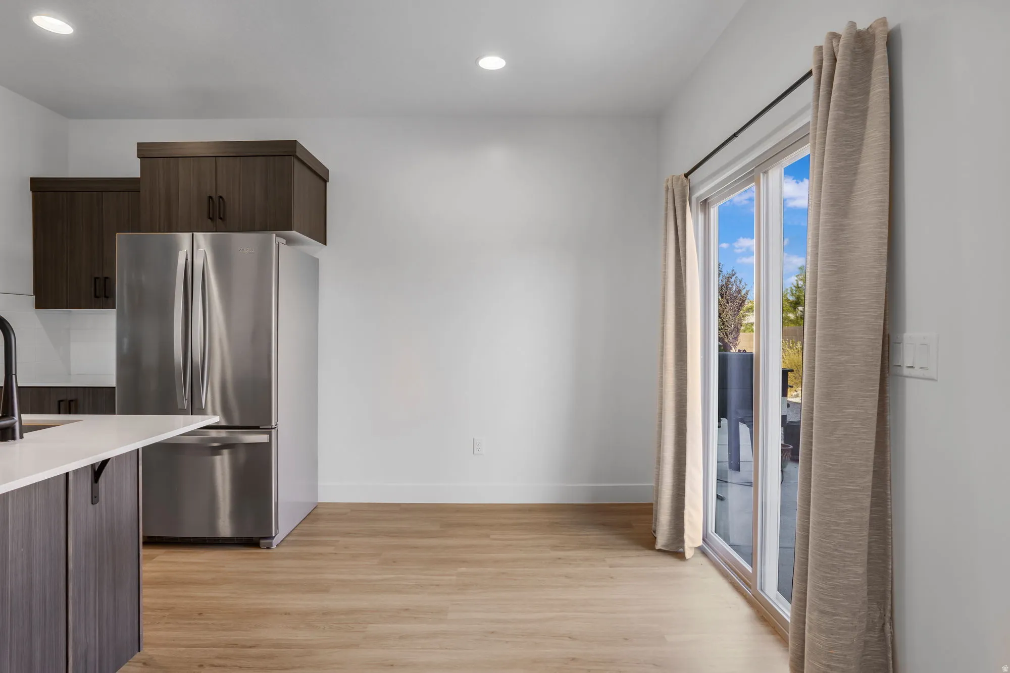 Kitchen and dining area featuring stainless steel French door refrigerator, dark wood-finish cabinetry, light wood-finish flooring, recessed lighting, and a sliding glass door
